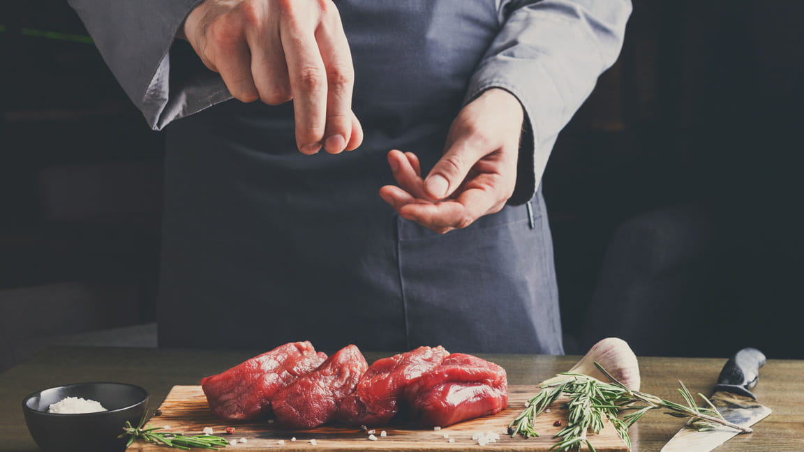 男人的手在烹饪时向肉中添加盐