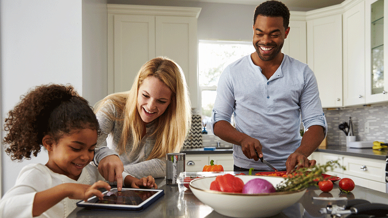多样化的家庭在厨房用餐和使用平板电脑