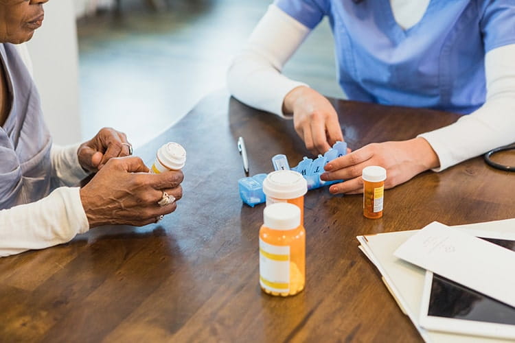 一位面目全非的女护士向一位老年病人展示如何将她的药物整理成每日药片